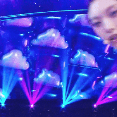 a woman is standing in front of a stage with clouds and lights