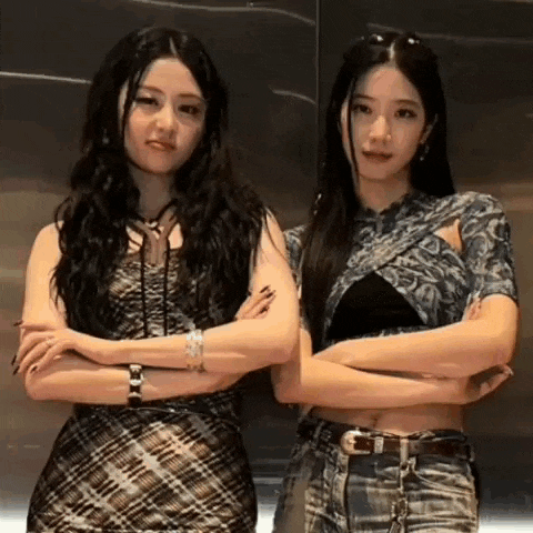 two women are standing next to each other with their arms crossed and looking at the camera .