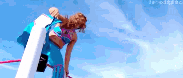 a woman in a blue dress is doing a trick on a pole .