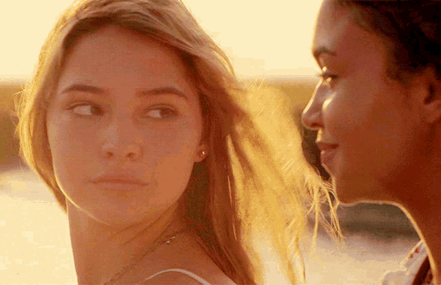 a close up of two women looking at each other with the sun shining on their faces