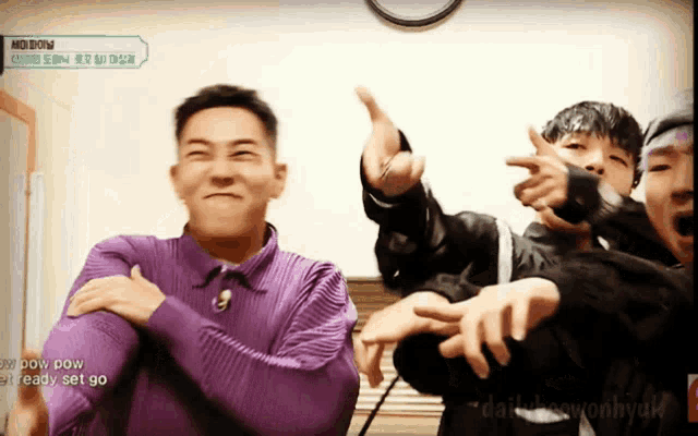 a man in a purple shirt is pointing at the camera