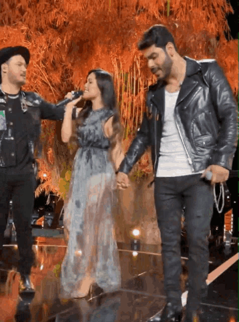 a man in a black leather jacket holds a woman 's hand while she sings into a microphone
