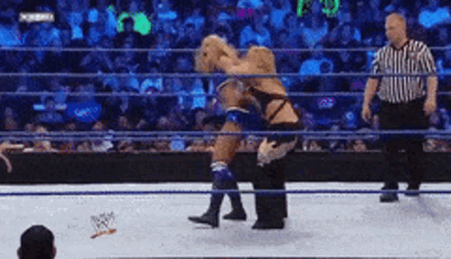 a wrestler is being lifted in the air by another wrestler while a referee looks on