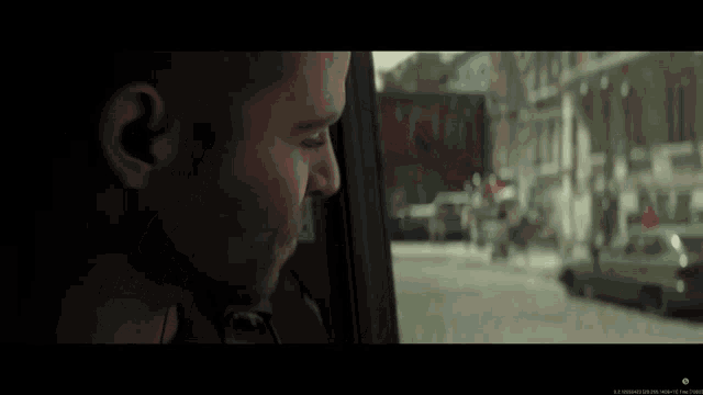 a man is looking out of a car window with a blurred image of a street behind him