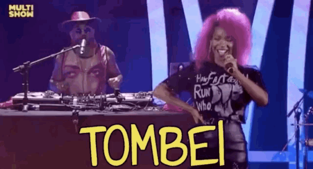 a woman with pink hair is singing into a microphone while a man in a cowboy hat is behind her