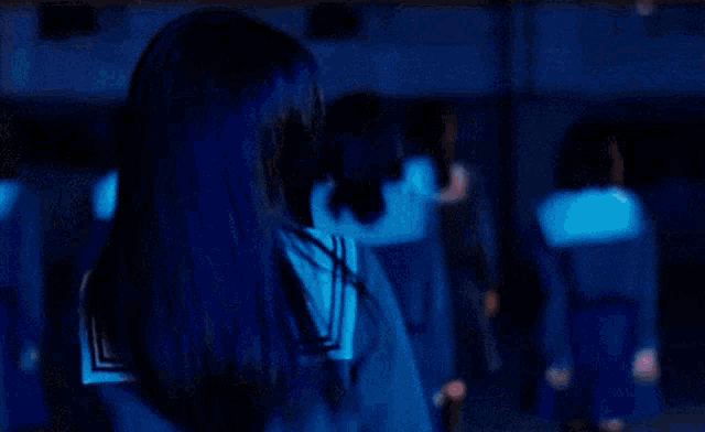 a girl with blue hair is holding a blue object in her hands in a dark room .
