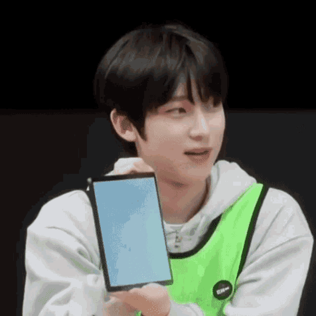 a young man in a green vest is holding a tablet and smiling .