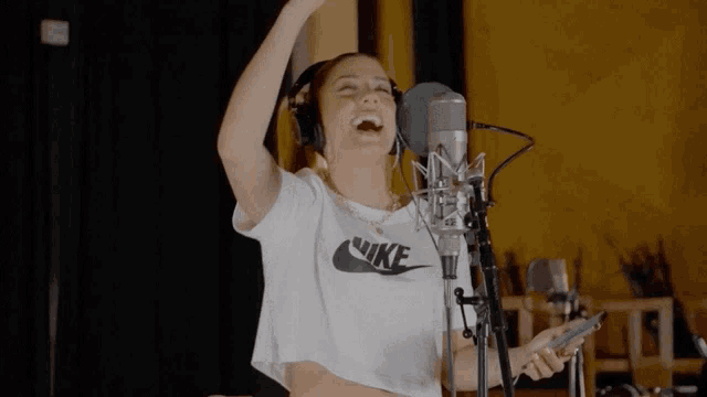 a woman wearing headphones and a white nike shirt sings into a microphone