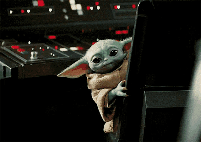a baby yoda from star wars is sitting in a chair looking out of a window .