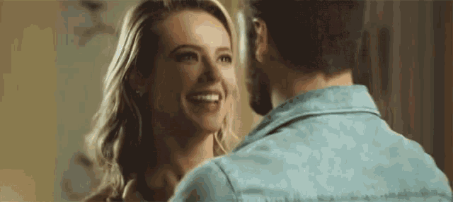 a man and a woman are looking at each other and smiling . the woman is wearing a blue shirt .