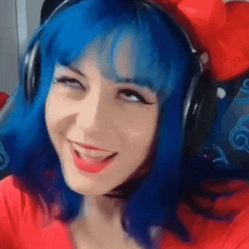 a woman with blue hair is wearing headphones and a red shirt and smiling .