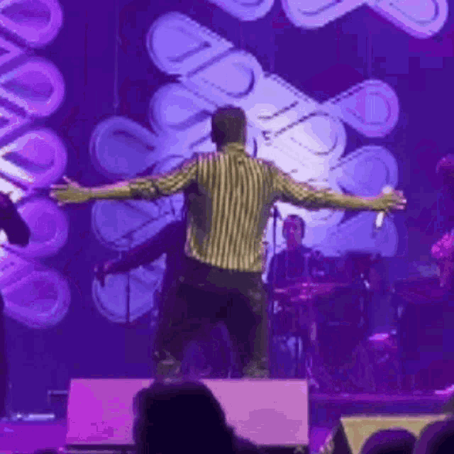 a man with his arms outstretched on a stage with a purple background