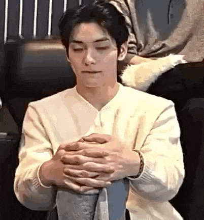 a young man is sitting in a chair with his hands folded in front of his chest .