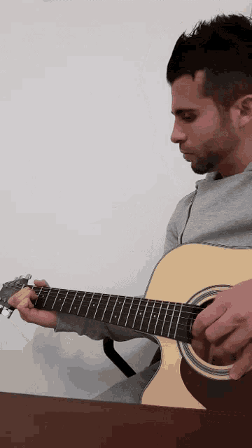 a man is playing an acoustic guitar while sitting at a desk