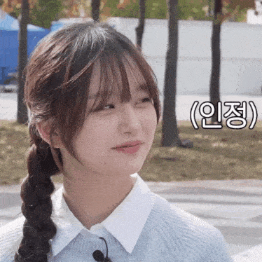 a girl with a braided ponytail looks at the camera in front of a foreign language sign