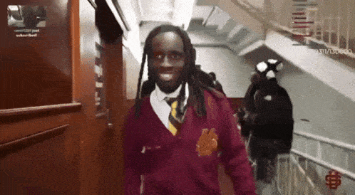 a man in a maroon sweater and tie is walking down stairs