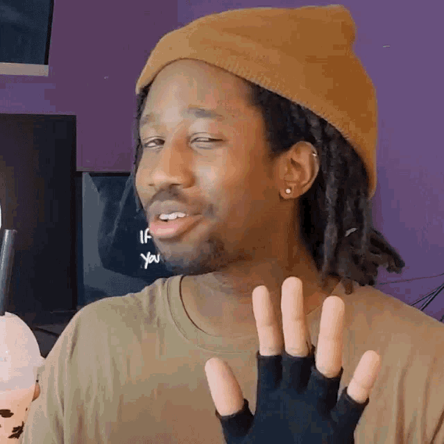 a man wearing a beanie and a glove is making a face