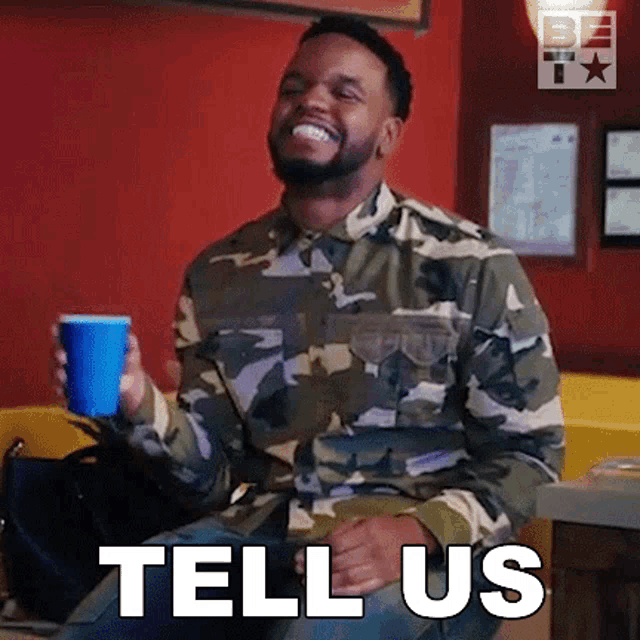 a man in a camouflage shirt is holding a blue cup and smiling while sitting in a chair .