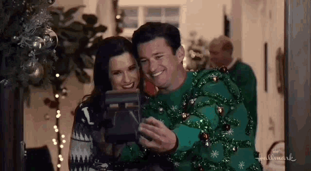 a man and a woman are taking a selfie together while wearing ugly sweaters .