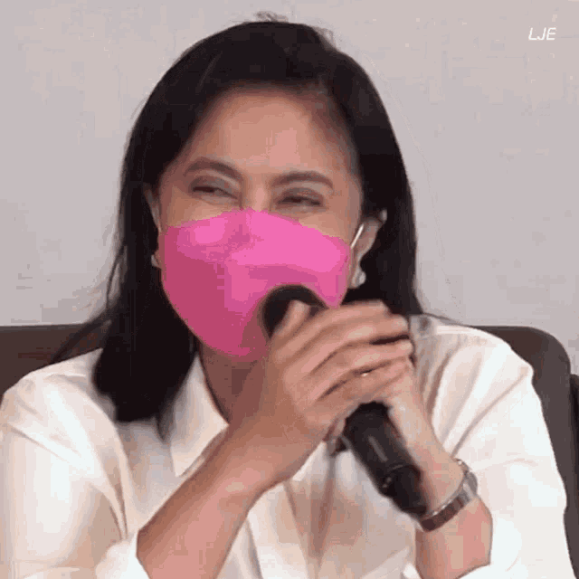 a woman wearing a pink mask is talking into a microphone .