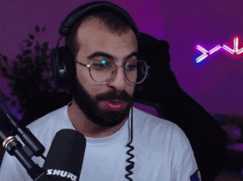 a man wearing headphones and a shure microphone looks at the camera
