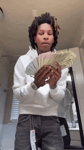 a man in a white hoodie holds a bunch of money