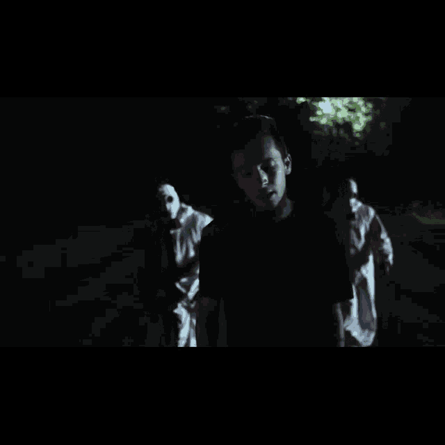 a man in a black shirt is standing in the dark with a group of people in white masks