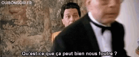 a man in a tuxedo is talking to another man in a room .