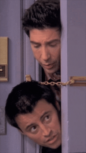 two men peeking out from behind a door with a chain around their necks