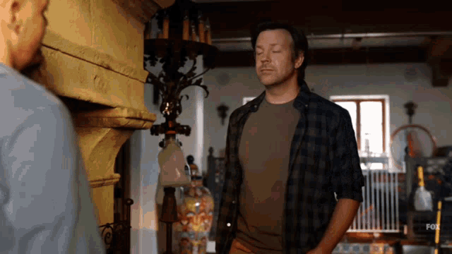a man in a plaid shirt stands next to another man in a room