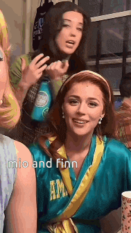 a group of women are posing for a picture and one of them is wearing a blue robe with the name mio and finn on it .
