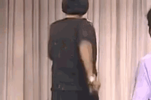 a man in a black hat is standing on a stage in front of a curtain .