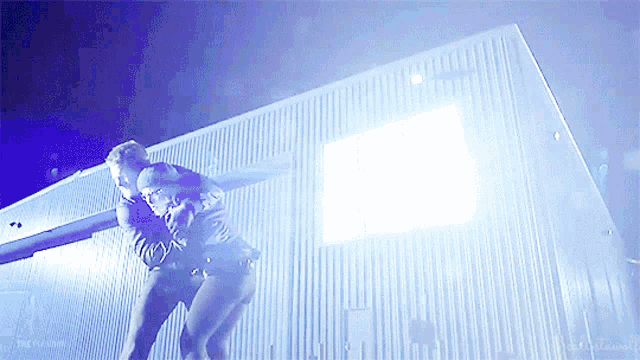 a man is standing in front of a building with a blue light coming out of it