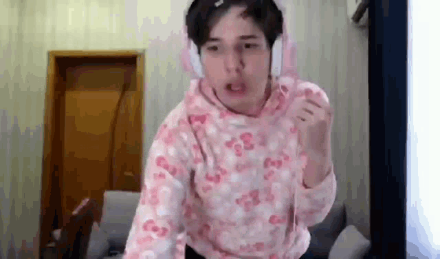 a young man wearing headphones and a pink sweater is standing in a room .