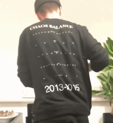 a man wearing a black shirt that says chaos balance on the back
