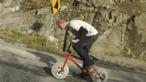 a man is riding a bike down a hill next to a yellow sign that says ' a ' on it