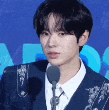 a young man is standing in front of a microphone with a tear coming out of his eye .