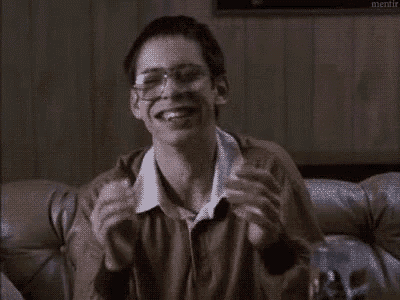 a young man wearing glasses is sitting on a couch eating a sandwich .