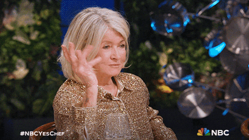 a woman in a gold sequined shirt is sitting at a table with a glass of wine in front of a nbc logo