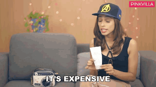 a woman sitting on a couch holding a piece of paper and says it 's expensive