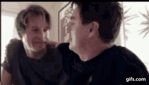 two men are sitting next to each other and looking at each other in a room .