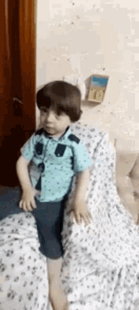 a little boy in a blue shirt is sitting on a white blanket on a bed .