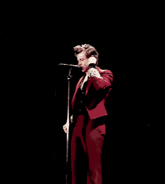 a man in a red suit is singing into a microphone on a stage
