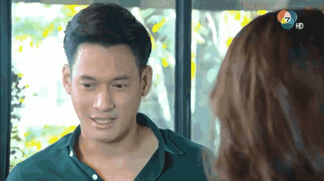 a man in a green shirt is talking to a woman with the number 7 on the screen behind him