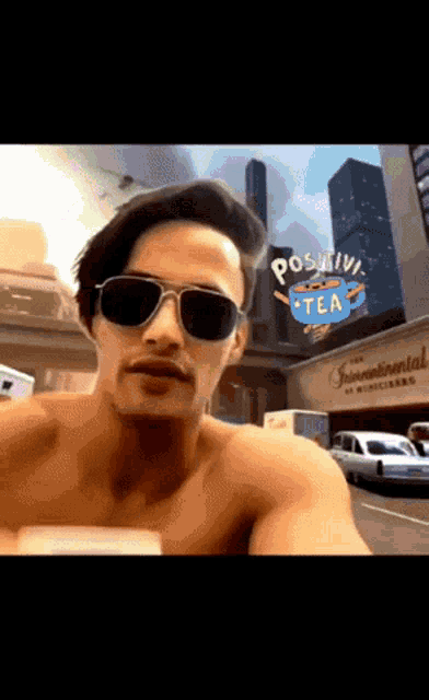 a shirtless man wearing sunglasses is standing in front of a sign that says " positive tea "