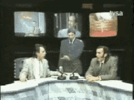 two men are sitting at a table in front of a tv with tvsa on it