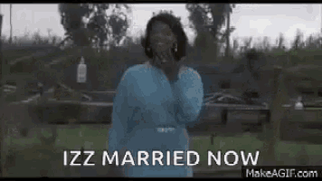 a woman in a blue dress is standing in front of a fence with the words `` izz married now '' written on it .