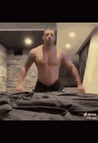 a shirtless man is standing on a bed in a room .