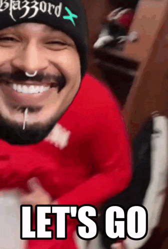 a man wearing a red sweater and a black beanie is smiling and says let 's go