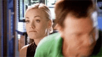 a woman is looking at herself in the mirror while a man looks on .